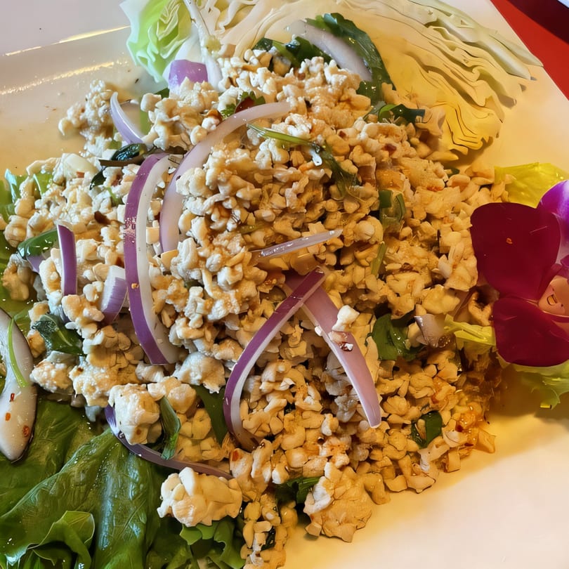 Thai Larb Gai, a minced chicken salad with red onions, green herbs, and cabbage on a white plate.